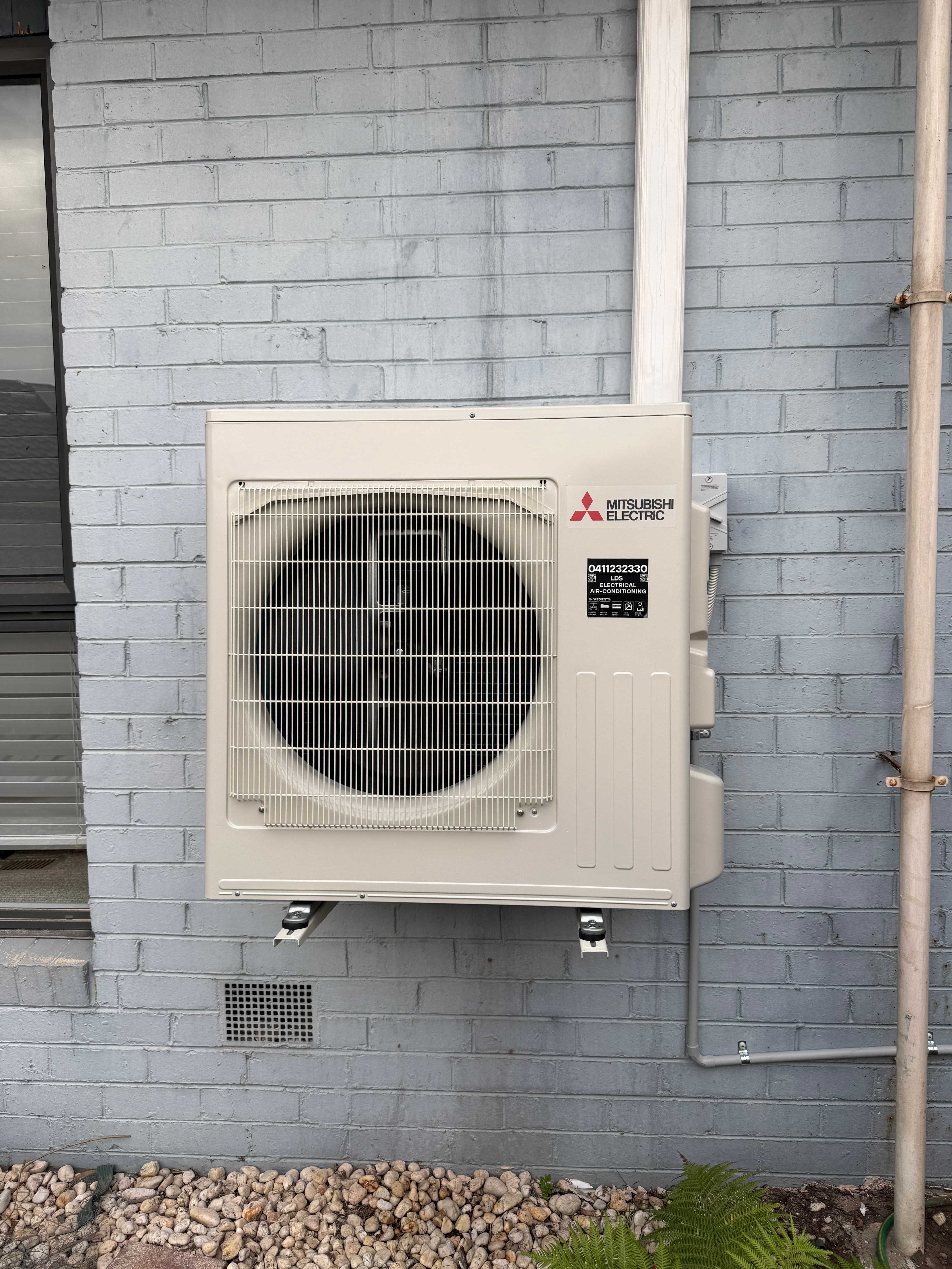 Wall-mounted outdoor Mitsubishi Electric air conditioning unit with pipework on a brick wall