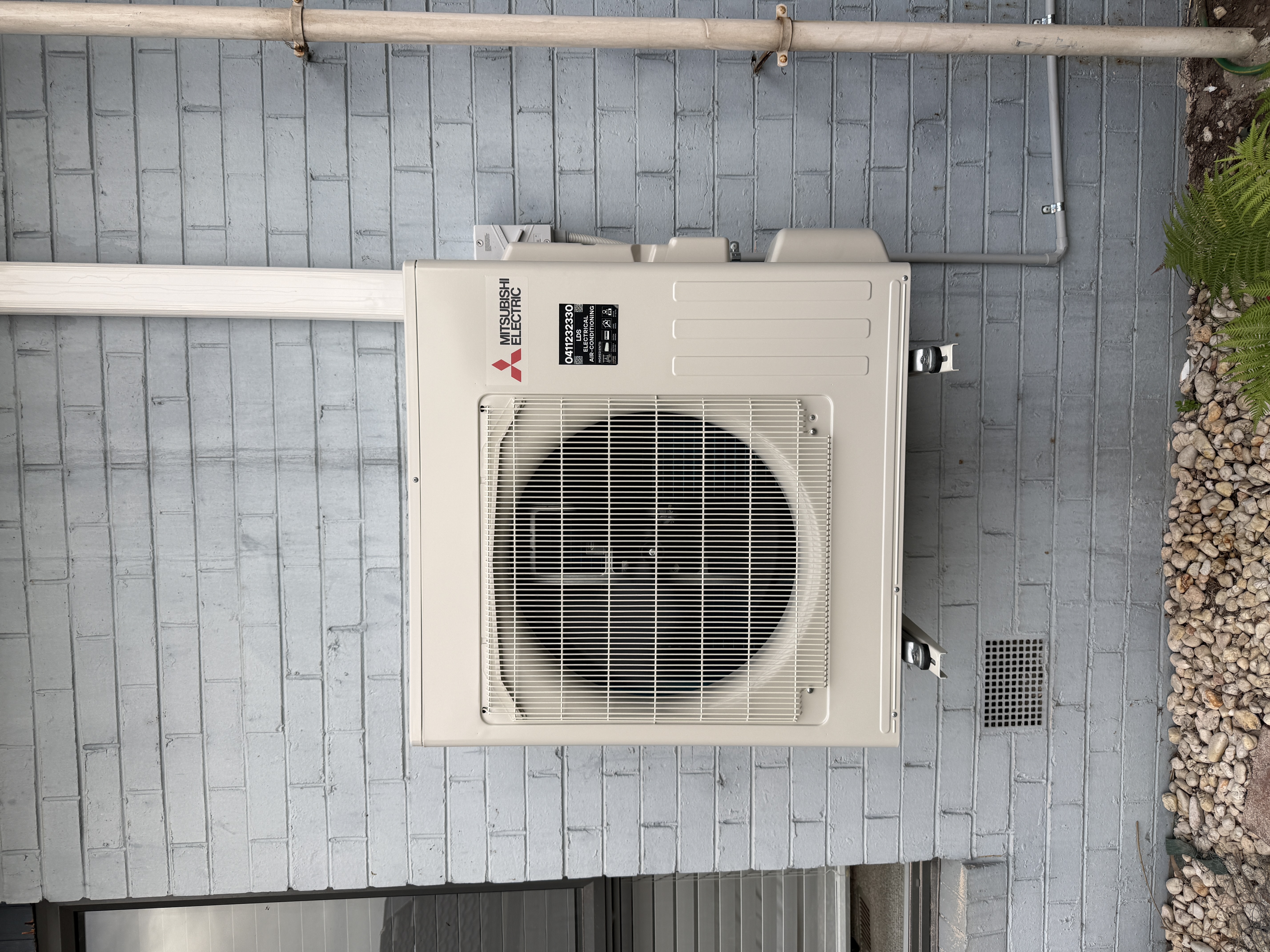 Outdoor Mitsubishi Electric air-conditioning unit mounted on an exterior brick wall.