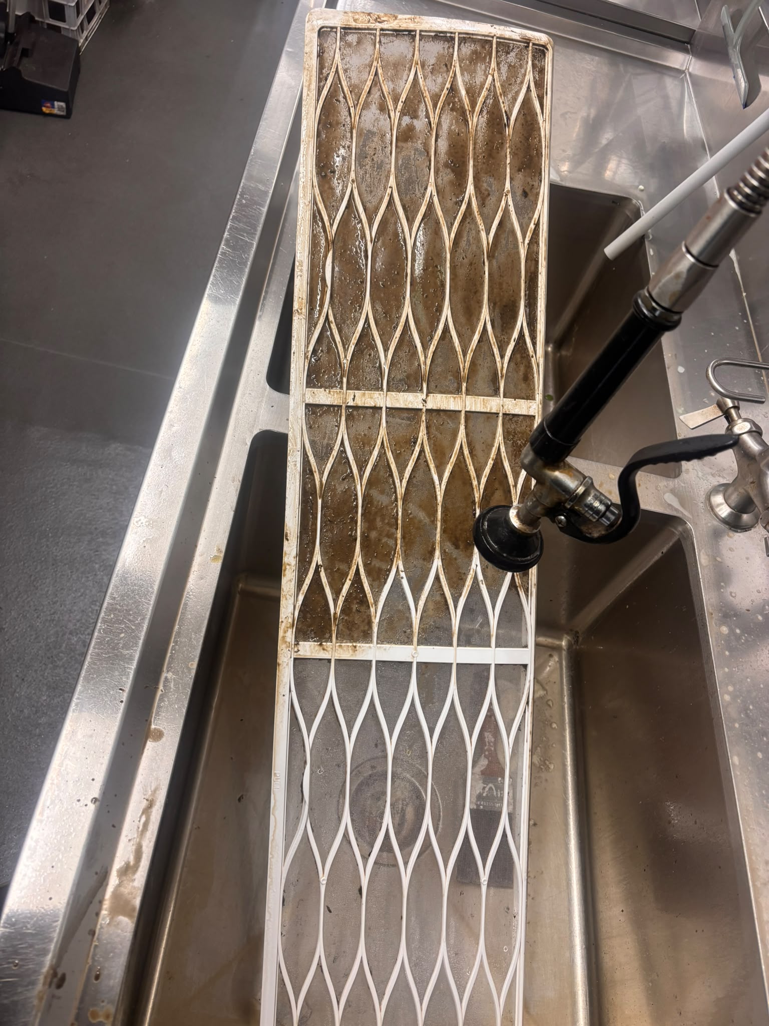 An air conditioner filter being rinsed in a stainless-steel sink.