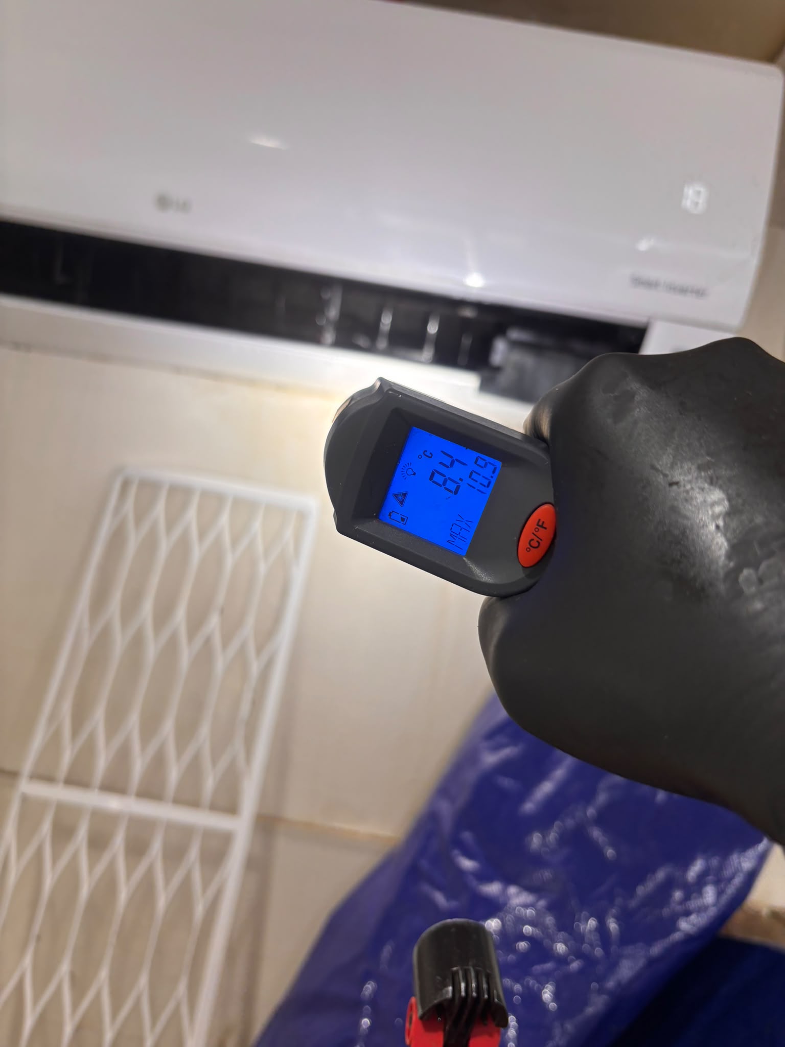 A handheld infrared thermometer aimed towards a wall-mounted indoor unit.